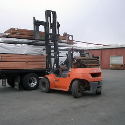 A tractor carefully loads redwood lumber on a truck for delivery.