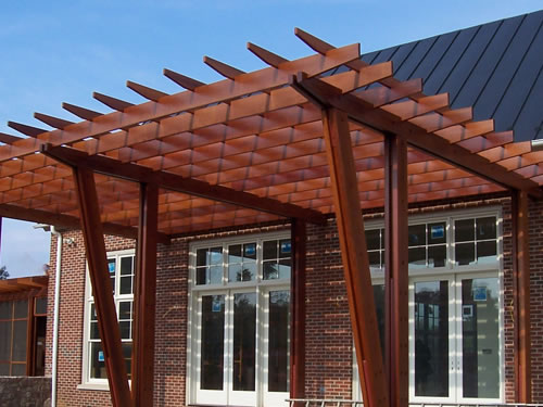 Redwood beams used in a handsome shade structure on the side of a home.